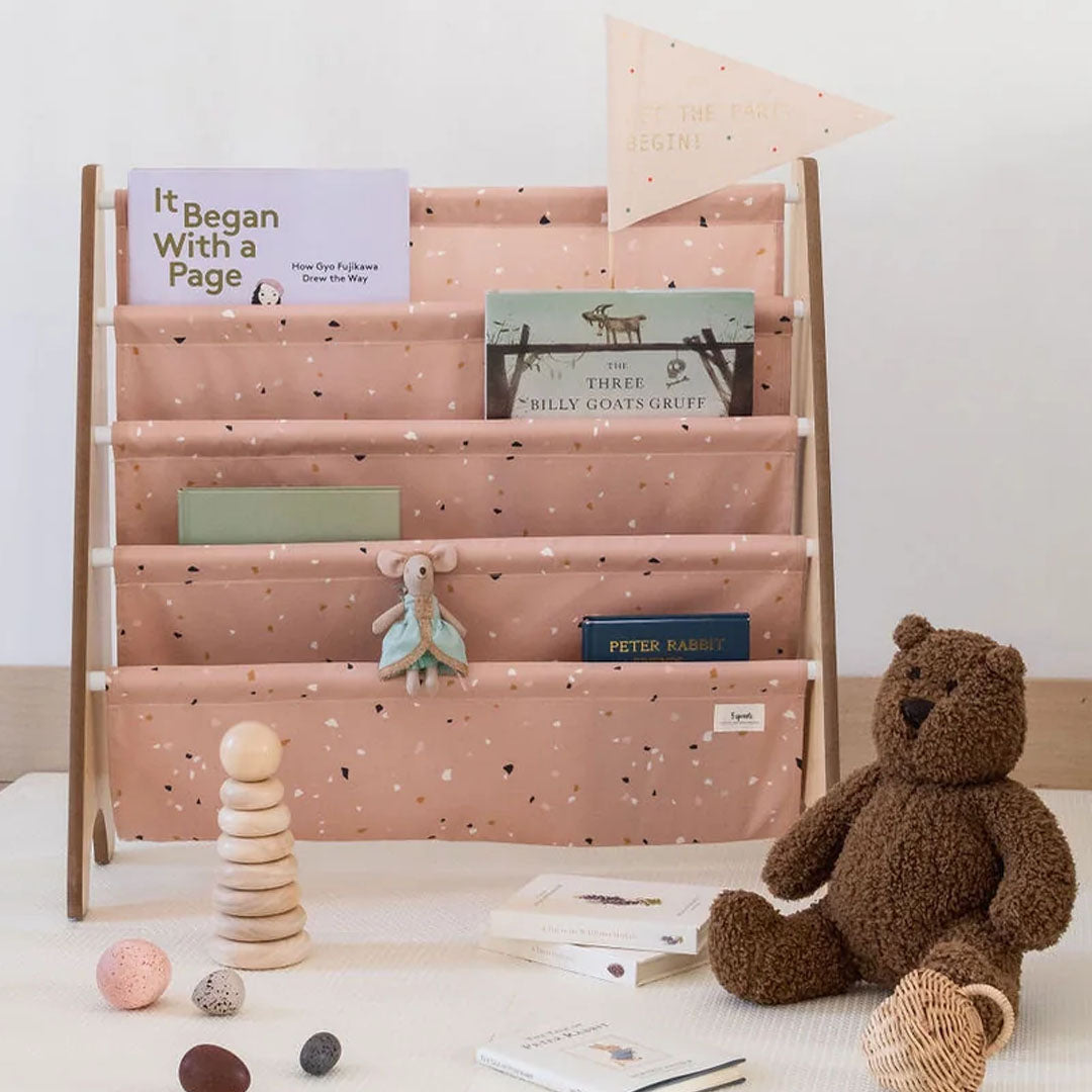 3 sprouts kinderboekenrek met roze terrazzo stof, gevuld met boeken en speelgoed.