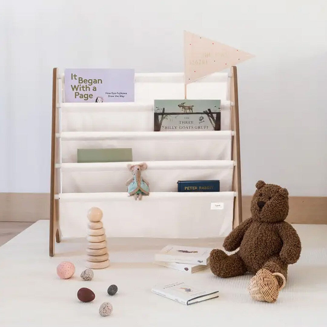 3 sprouts kinderboekenrek gevuld met boeken, met een teddybeer en speelgoed ervoor op de grond.