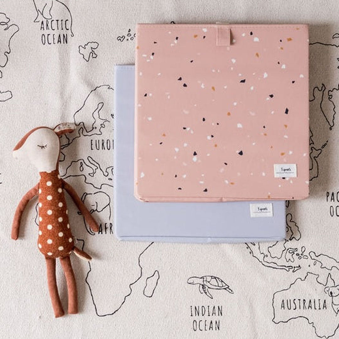 Twee gevouwen 3 sprouts opbergdozen, één roze terrazzo en één lichtblauw, naast een knuffelhert op een wereldkaartkleed.