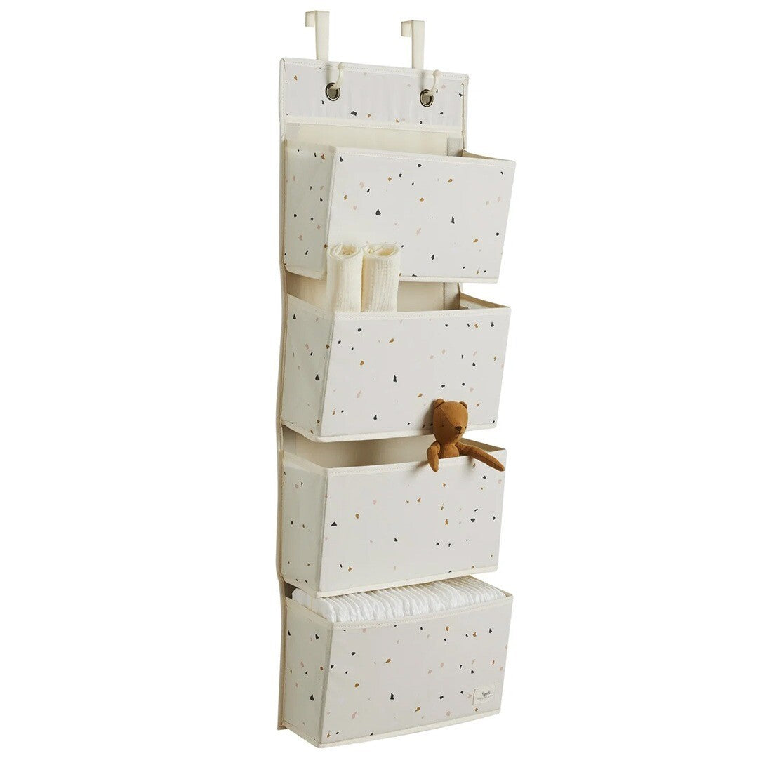 3 sprouts wandorganiser met terrazzo patroon, gevuld met babyspullen en een teddybeer, hangend aan witte haken.
