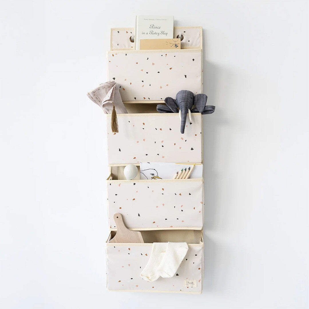 3 sprouts wandorganiser met terrazzo patroon, gevuld met een boek, speelgoed en andere spullen, hangend aan een witte muur.