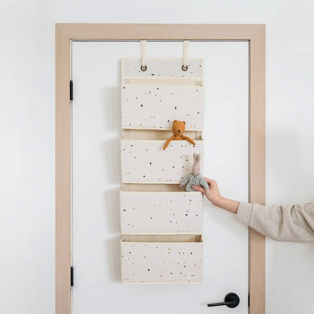 3 sprouts wandorganiser met terrazzo patroon hangend over een deur, met een hand die een konijn knuffel in een vakje plaatst.