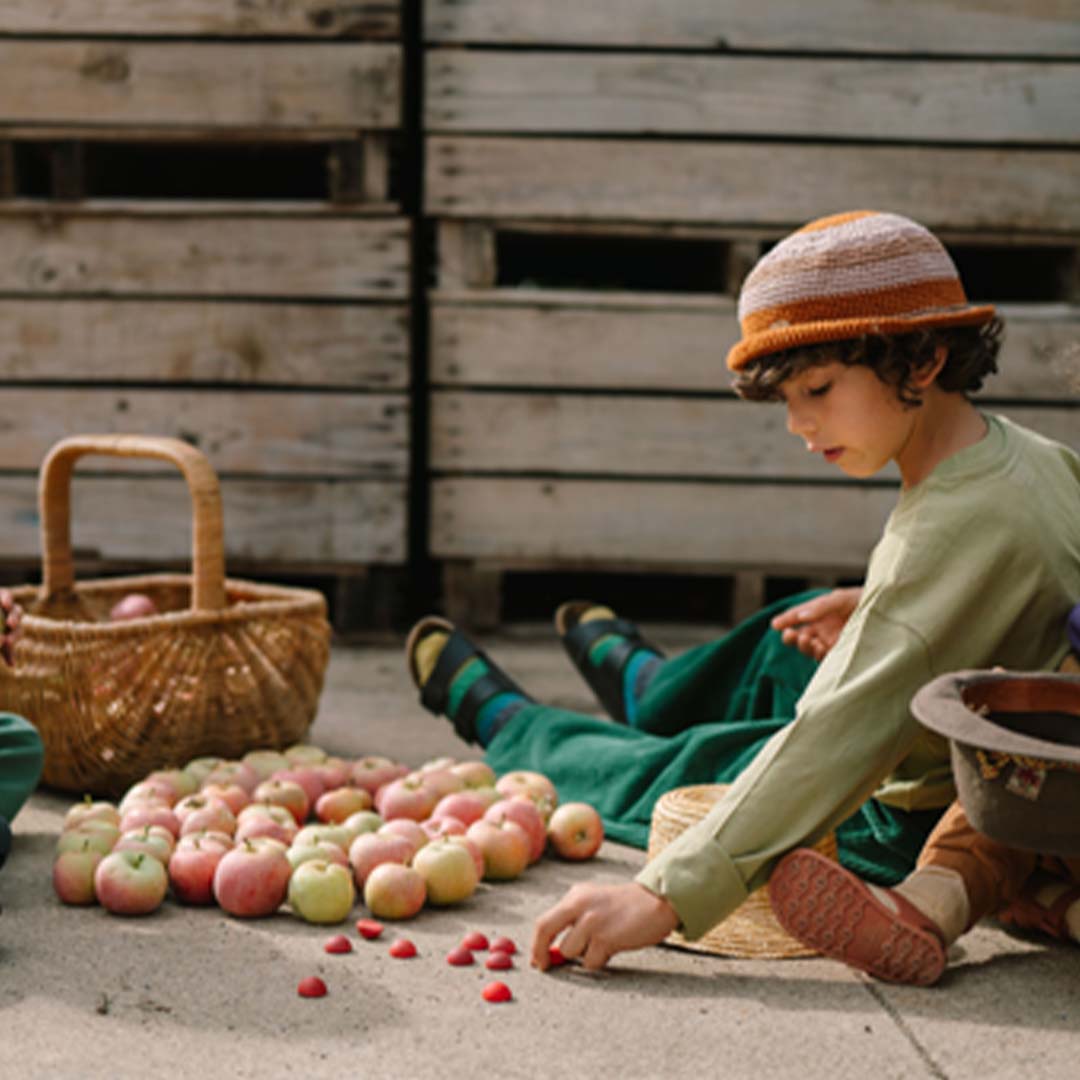 Een kind zit buiten en speelt met Grapat houten halve bollen en appels.