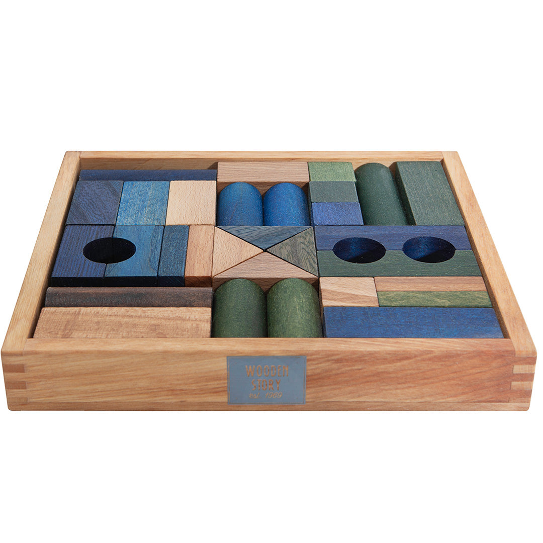 Wooden Story houten bouwblokken in blauw, groen en naturel, gerangschikt in een houten kist, schuin van voren gefotografeerd.