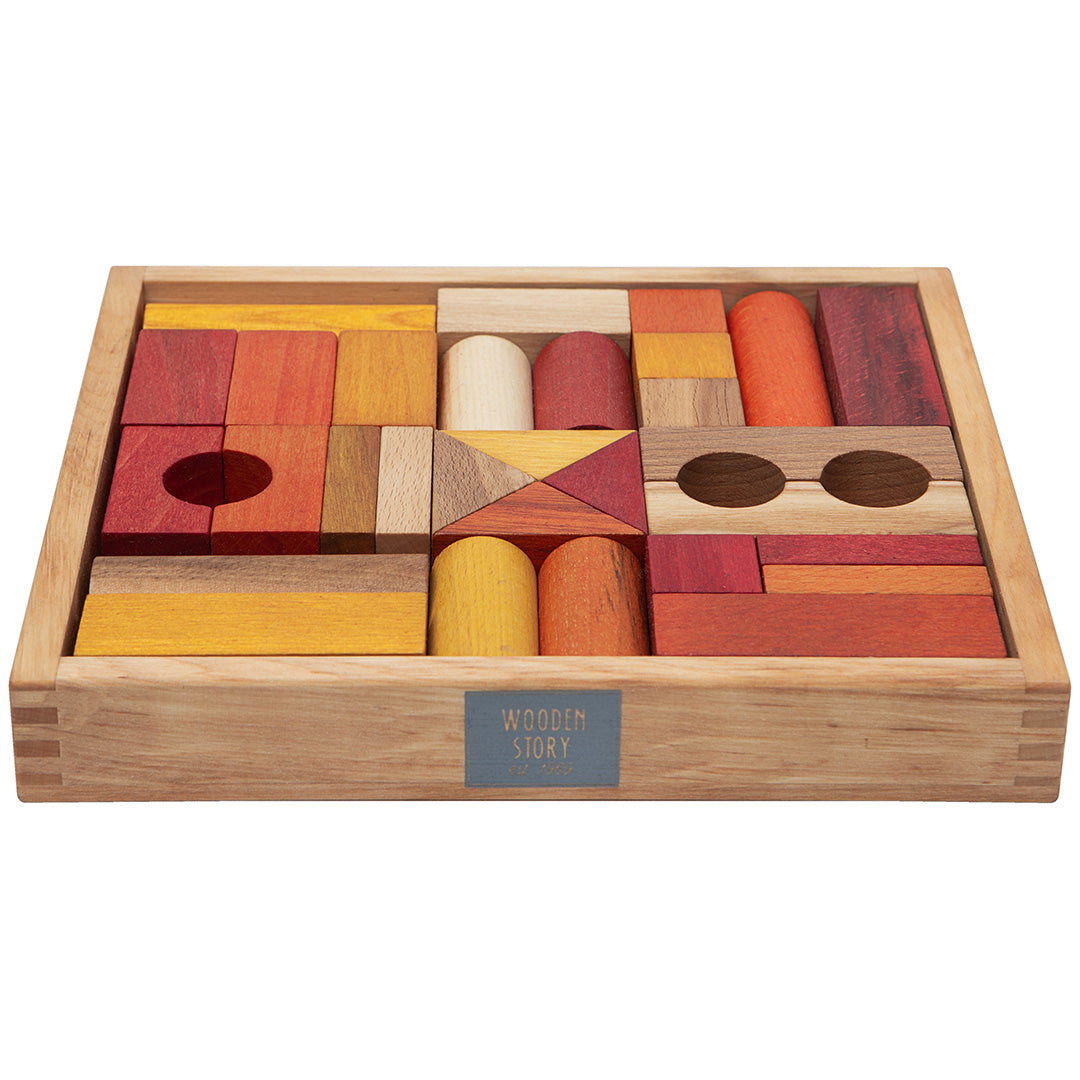 Wooden Story houten bouwblokken in warme kleuren, gerangschikt in een houten kist met het merklogo op de voorkant.