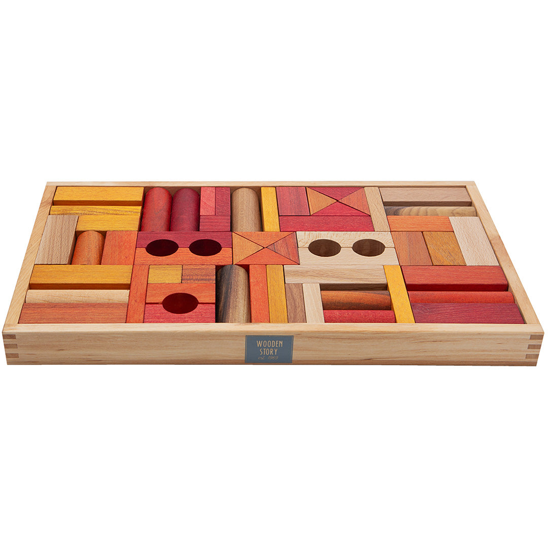 Wooden Story houten bouwblokken in warme tinten rood, oranje en naturel, gerangschikt in een houten bak, schuin van bovenaf gefotografeerd.