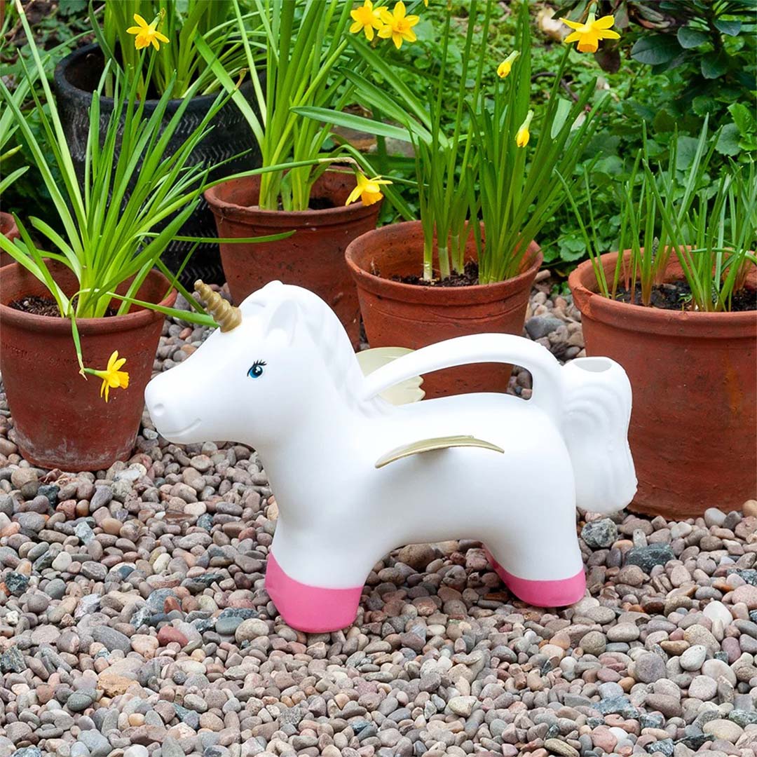 Eenhoorn gieter op grind in een tuin met potplanten en gele bloemen.