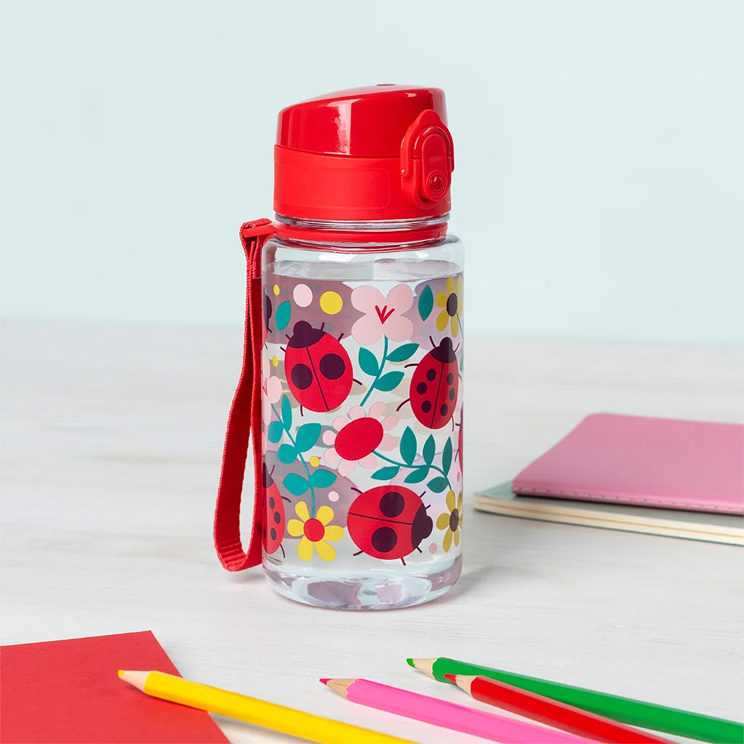Rex London kinder drinkfles met lieveheersbeestjes en bloemen op een bureau met kleurpotloden.