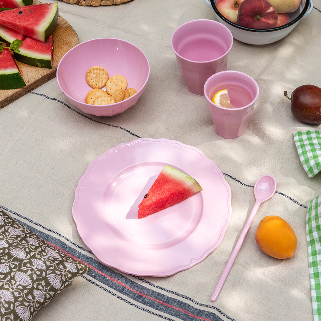 Een picknicktafel met een Rex London roze melamine kinderbord, bijpassende kom en bekers, en fruit.