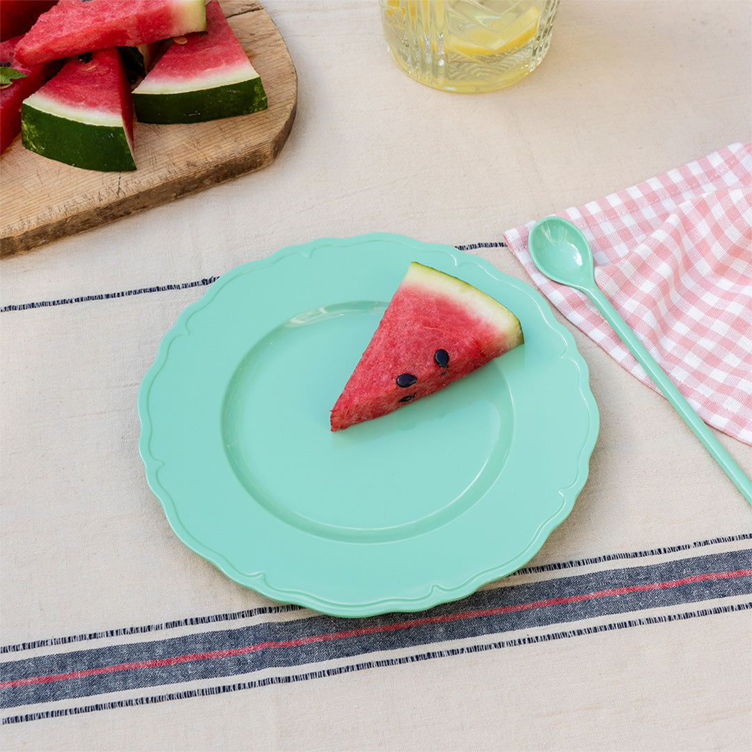 Rex London melamine kinderbord met een stuk watermeloen, liggend op een gestreept tafelkleed.
