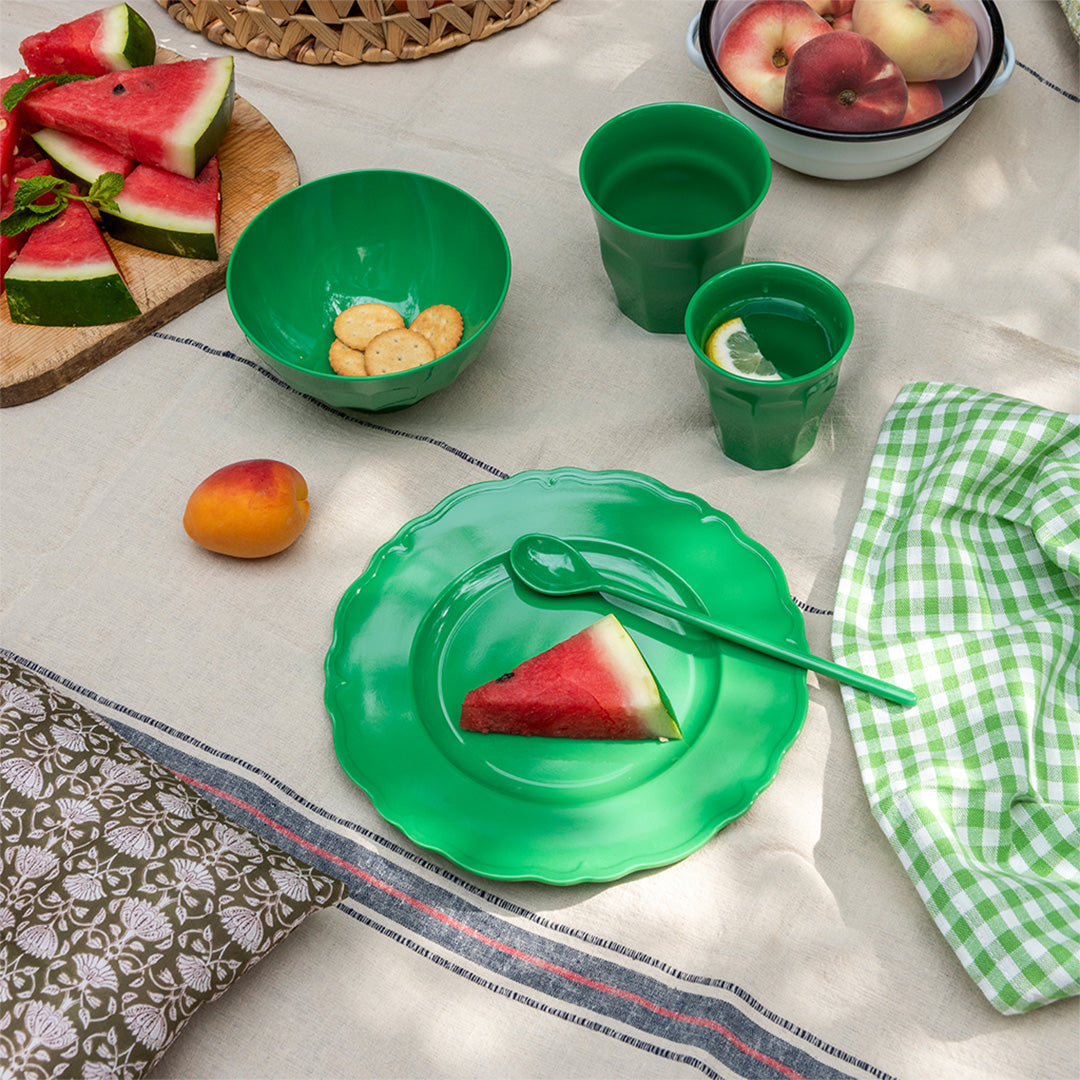 Een picknicktafel met het felgroene kinderbord, bijpassende kom en bekers, en fruit.