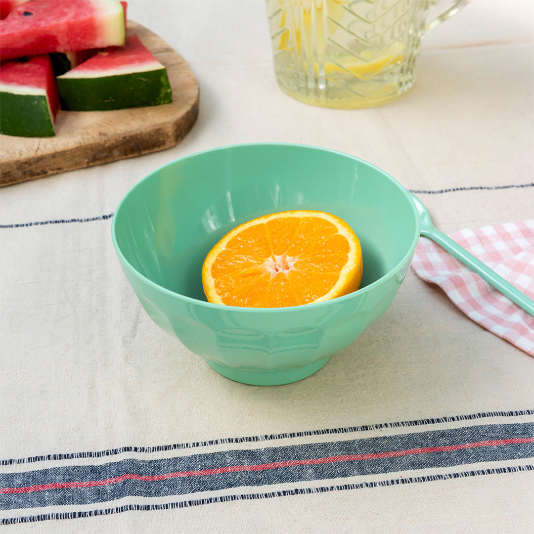 Rex London melamine kom in pistachegroen met een halve sinaasappel, op een tafel met fruit en drinken.