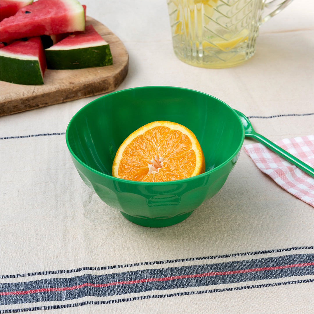 Groene melamine kom met een halve sinaasappel op een tafel met fruit.