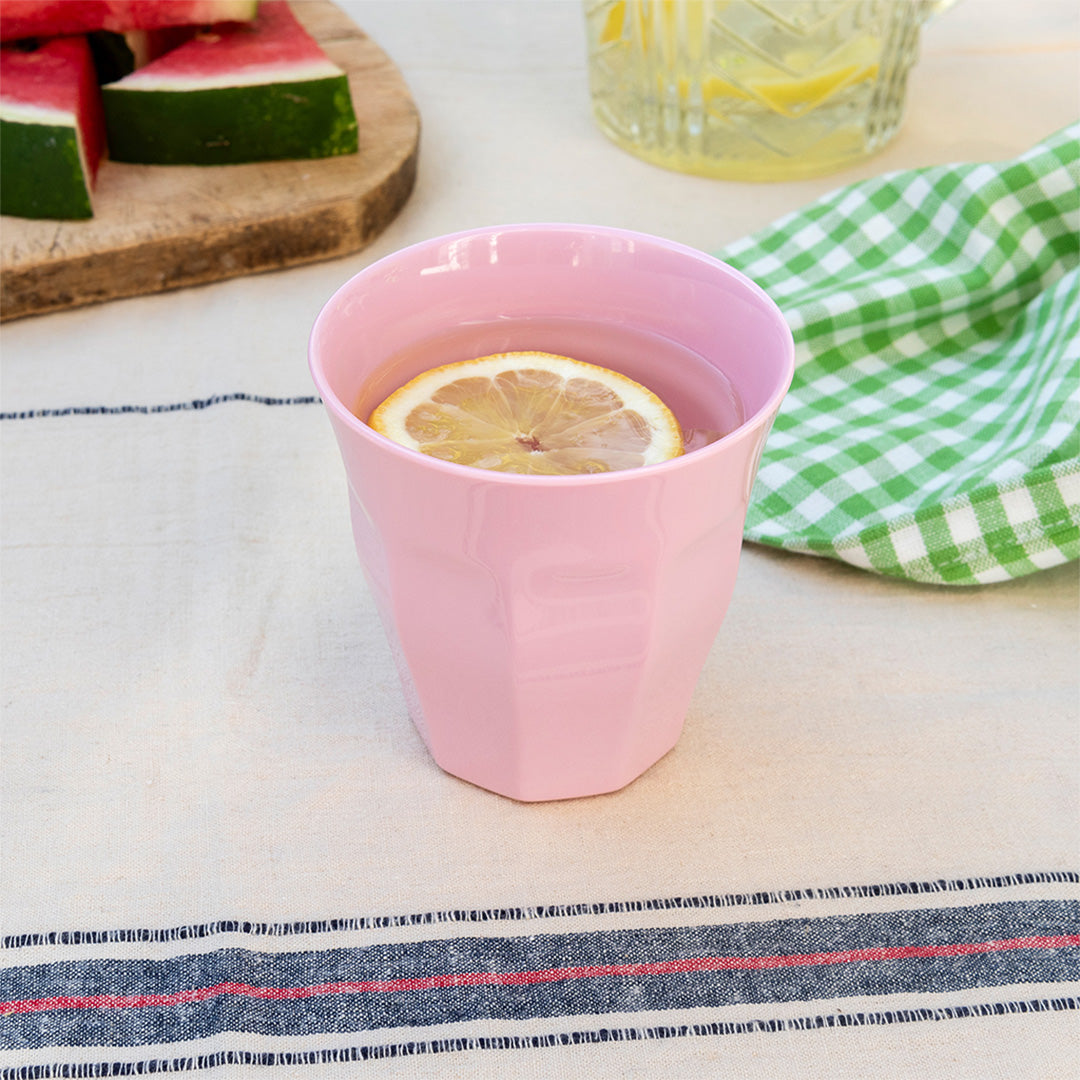 Roze melamine kinderbeker met water en een schijfje citroen op een tafelkleed.