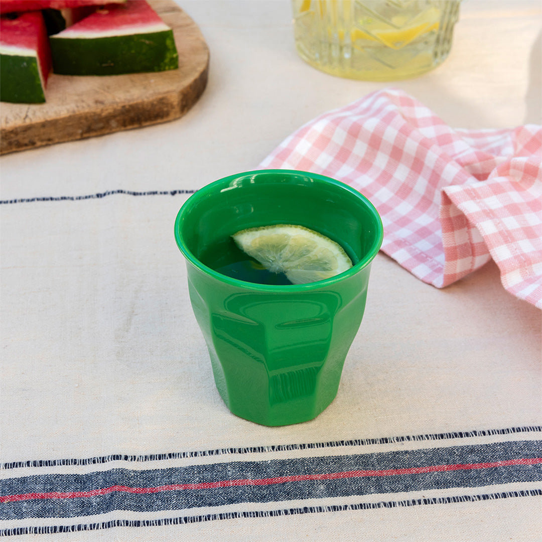 Groene kinderbeker met een schijfje citroen op een gestreepte picknickkleed.
