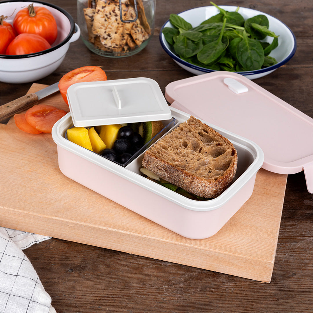 Rex London roze broodtrommel open op een houten plank, gevuld met een boterham en fruit.