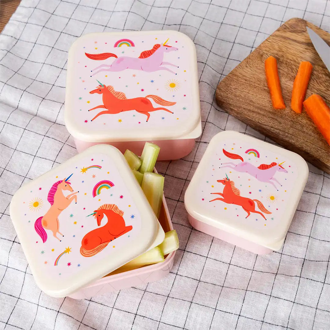 Drie Rex London snackdoosjes voor kinderen met eenhoorn-thema, waarvan één open met selderij, op een geruite doek.