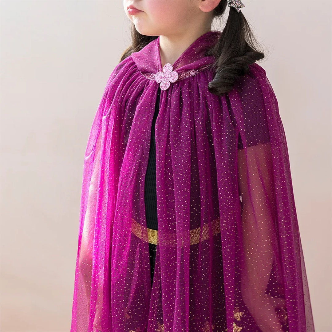 Zijaanzicht van een kind dat de Rex London donkerroze glitter verkleedcape draagt, met een bloemvormige sluiting.