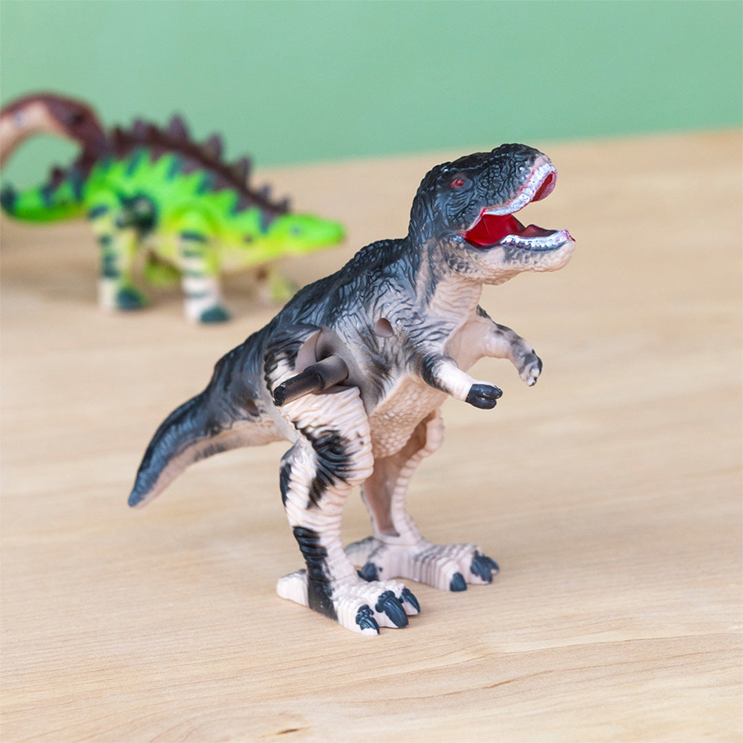 Opwindspeelgoed dino Tyrannosaurus Rex op een houten ondergrond met een groene dino op de achtergrond.