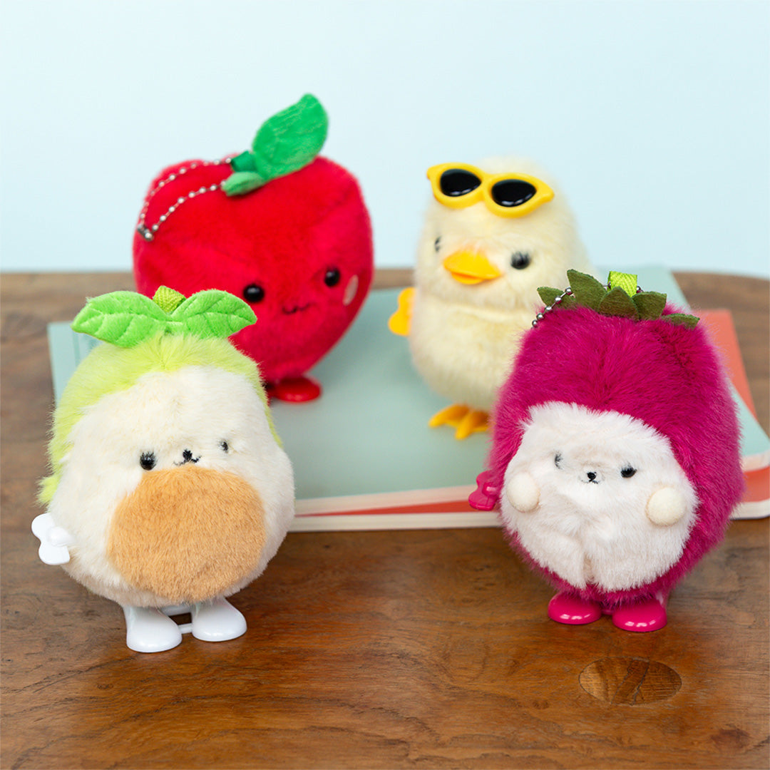 Collectie van vier pluizige opwindspeeltjes: een rode appel, een gele kuiken, een witte radijs en een paarse vrucht.