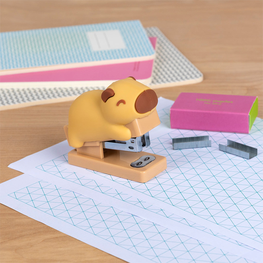 Rex London beige capybara mini nietmachine op een vel papier met losse nietjes.