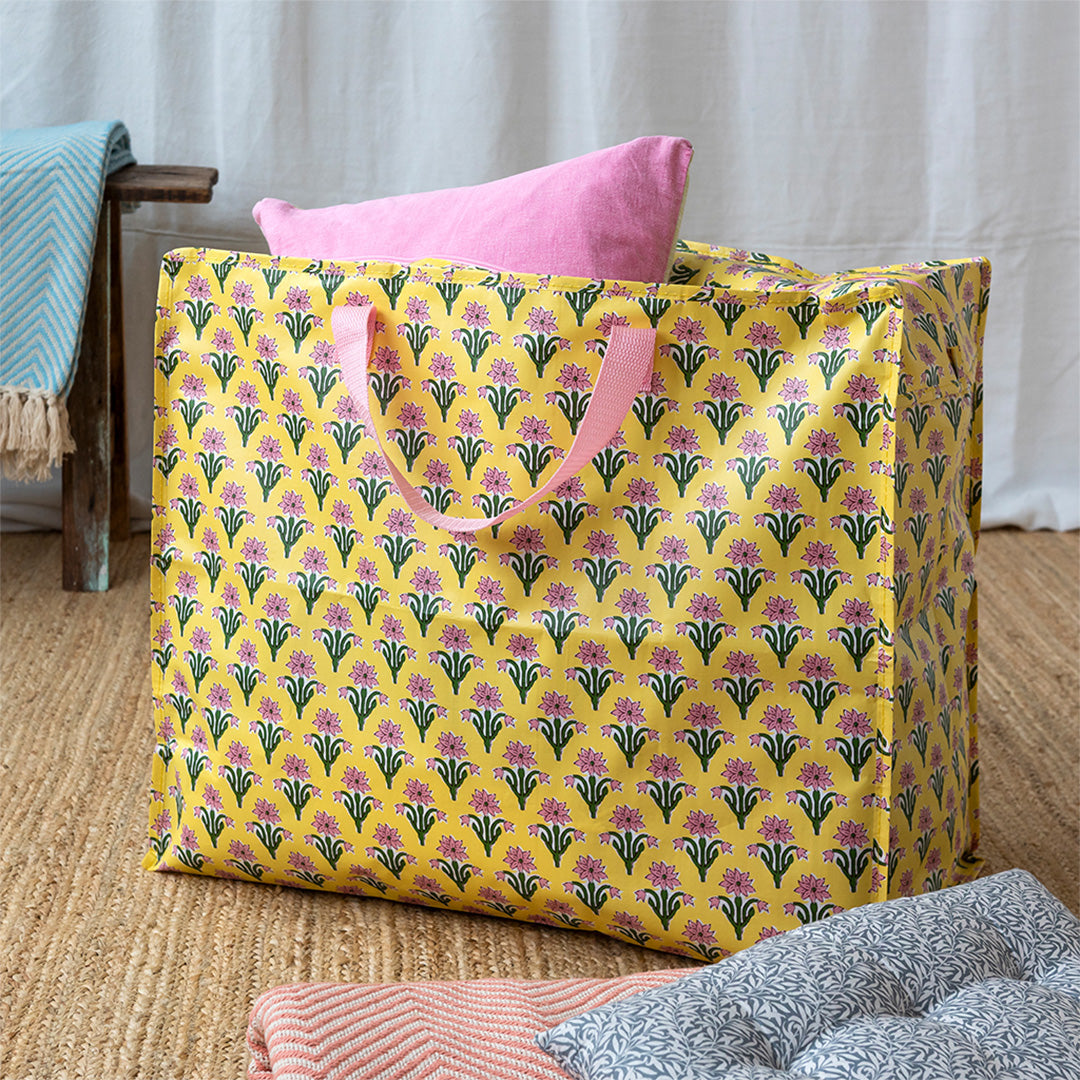 Rex London jumbo opbergtas met geel bloemenpatroon, gevuld met een roze kussen, staand op een vloerkleed.