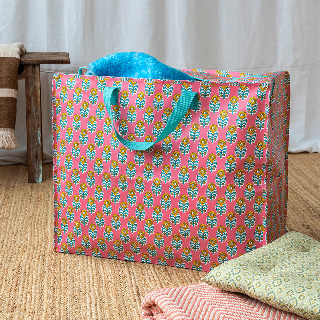 Gebloemde opbergtas op een vloerkleed, gevuld met een blauw item en met textiel ernaast.