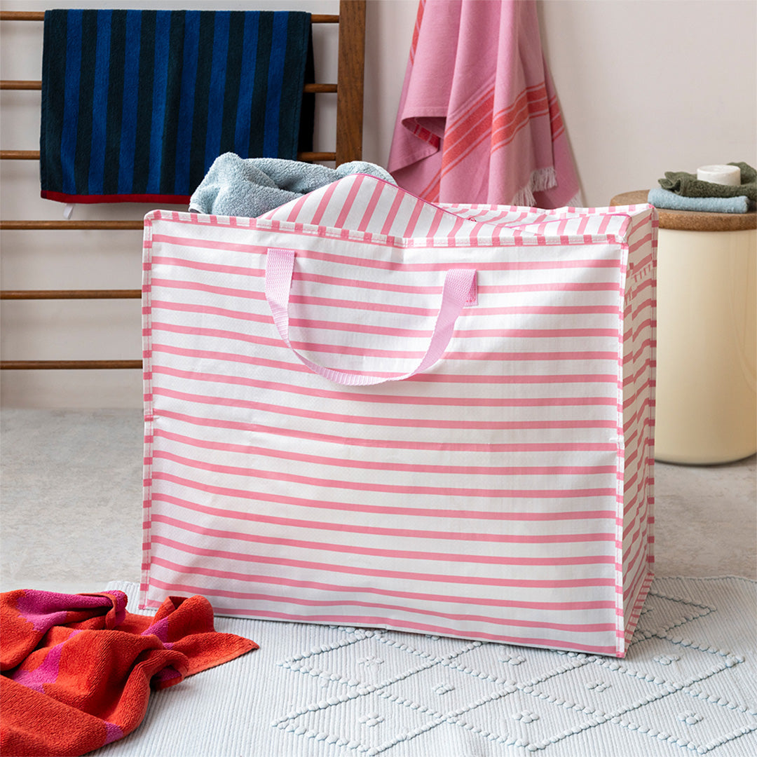 Rex London jumbo opbergtas met roze en witte strepen, gevuld met handdoeken in een badkamer.
