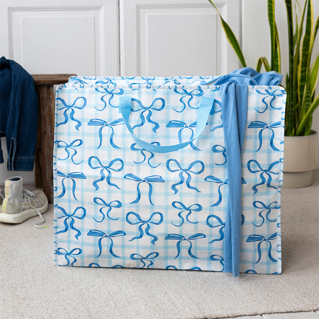 Rex London jumbo opbergtas met blauwe strikken en geruit patroon, gevuld met kleding in een kamer.