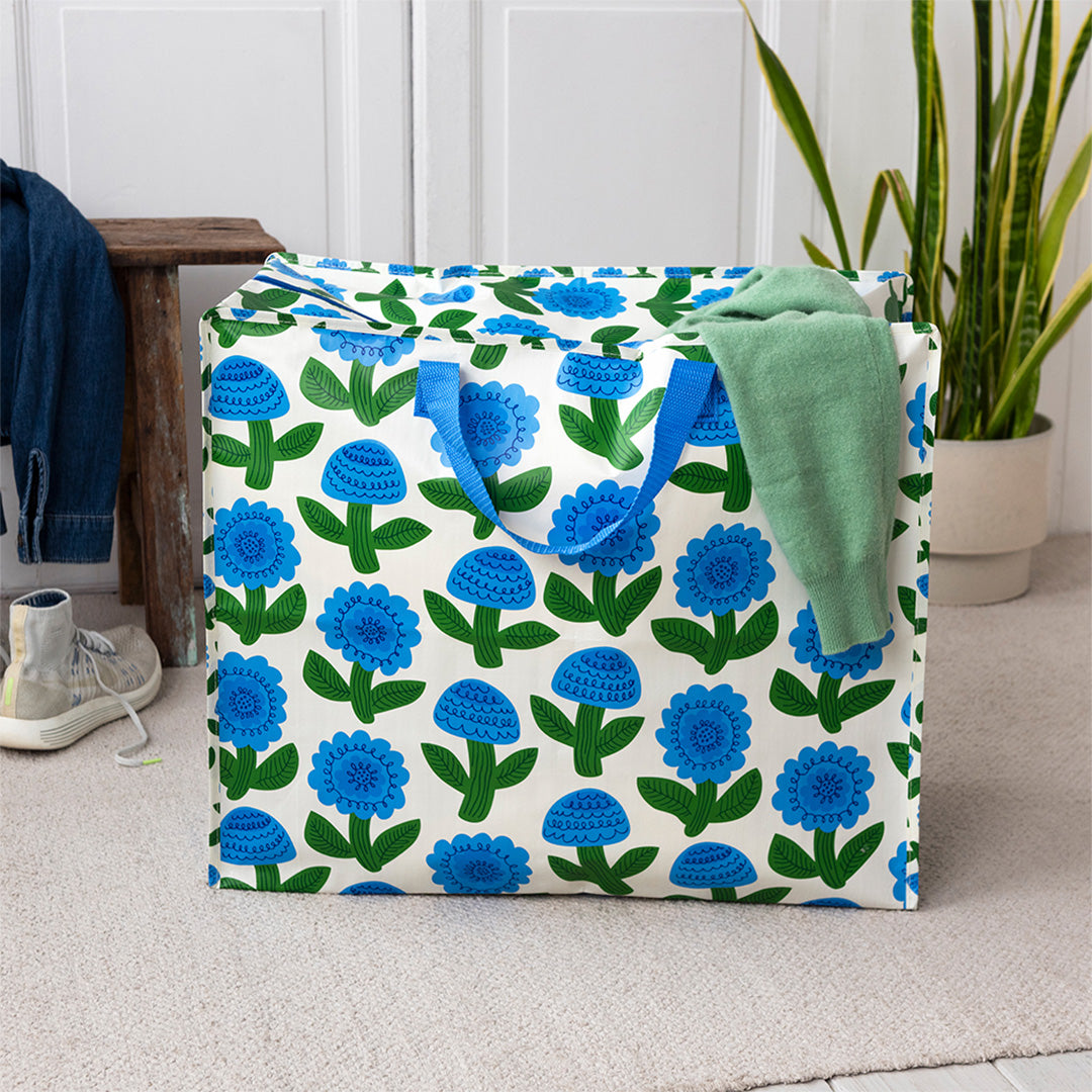 Rex London jumbo opbergtas Florence met blauw bloemenpatroon staat in een kamer met kleding.