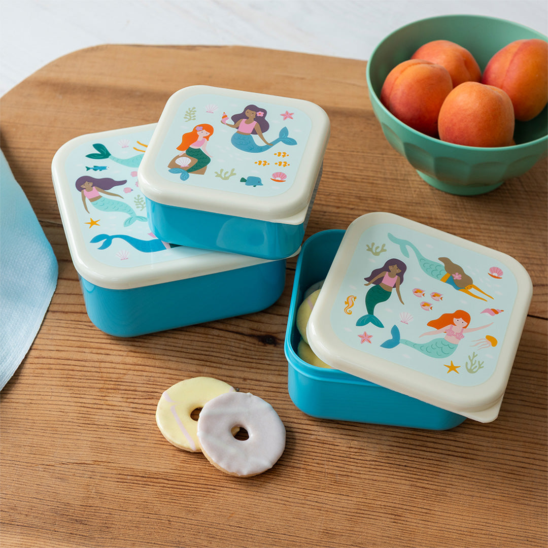 Rex London snackdoosjes met zeemeerminnenpatroon op een houten ondergrond, met koekjes en een kom perziken.