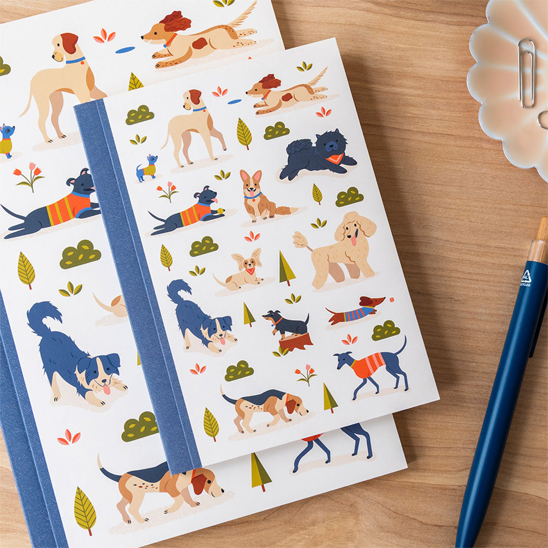 Twee Rex London A6 notitieboekjes met hondenillustraties, liggend op een houten tafel naast een pen.