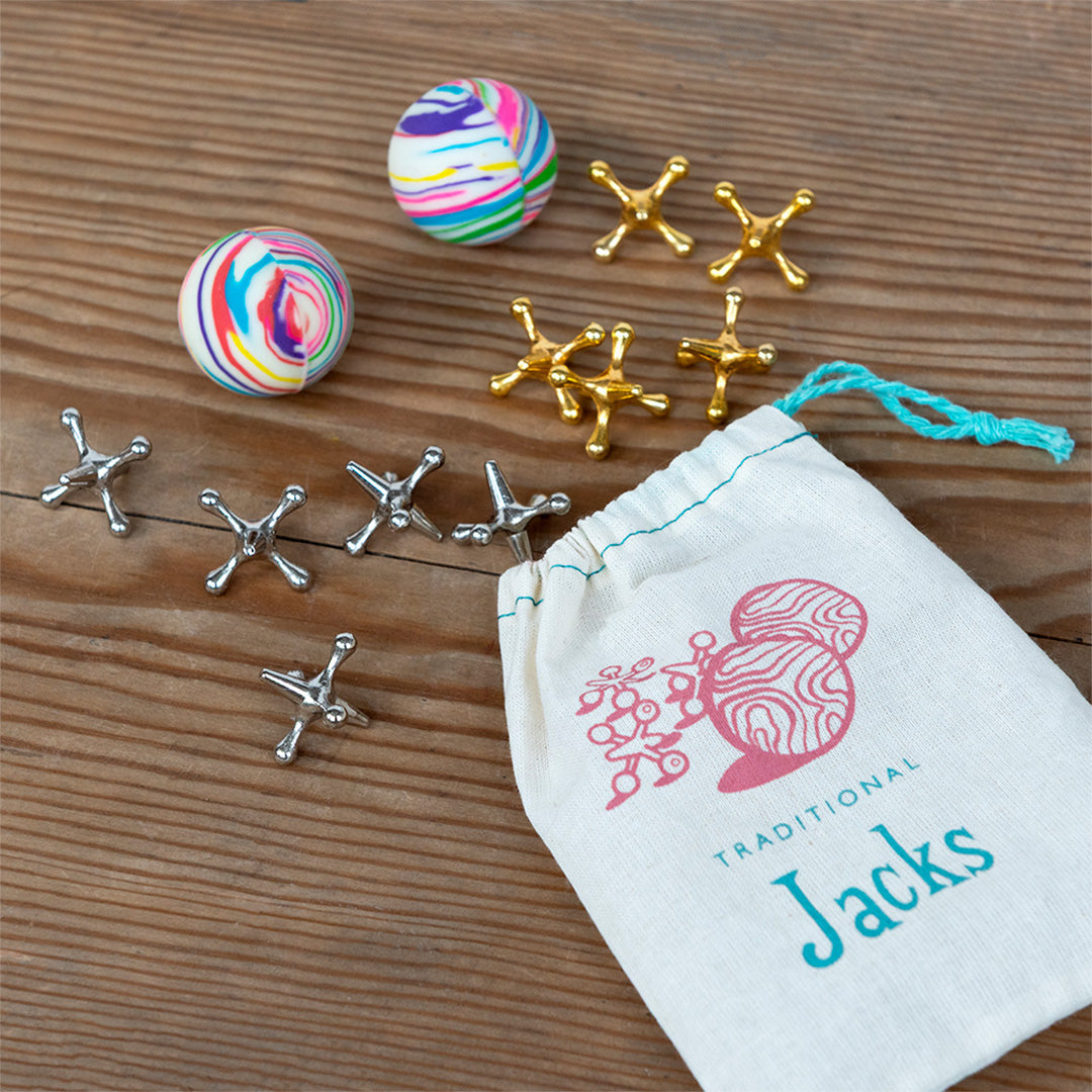 Rex London Traditional Jacks behendigheidsspel met een katoenen zakje, twee veelkleurige stuiterballen en gouden en zilveren metalen jacks op een houten ondergrond.
