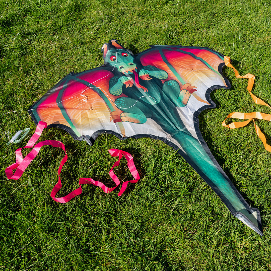 De rex london drakenvlieger ligt op groen gras, met roze en oranje linten.