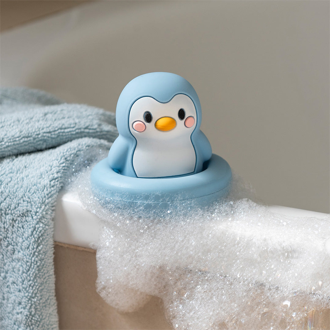 Rex London blauw siliconen pinguïn badspeeltje drijvend in badschuim op de rand van een bad.