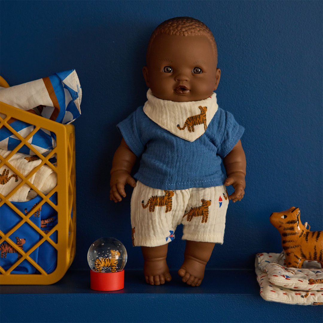 Een baby pop met tijgerkleding staat naast een le petit souk sneeuwbol met tijger en een tijgerspeeltje op een blauwe plank.