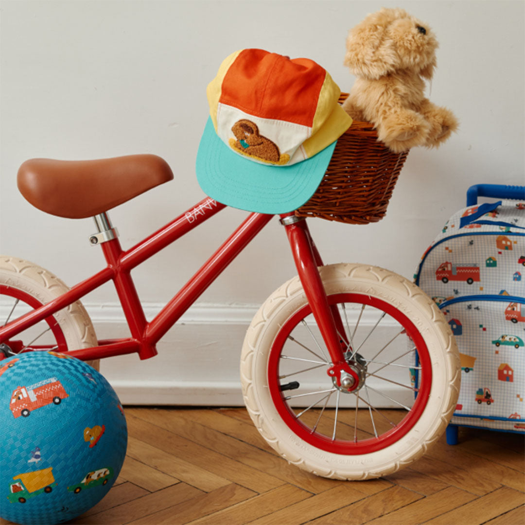 le petit souk kinderkoffer met voertuigenpatroon staat in een kinderkamer naast een rode loopfiets en een bal.