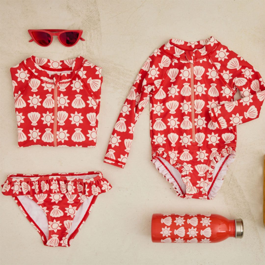 Collectie van le petit souk rode zwemkleding, zonnebril en waterfles met schelp- en zonpatroon.
