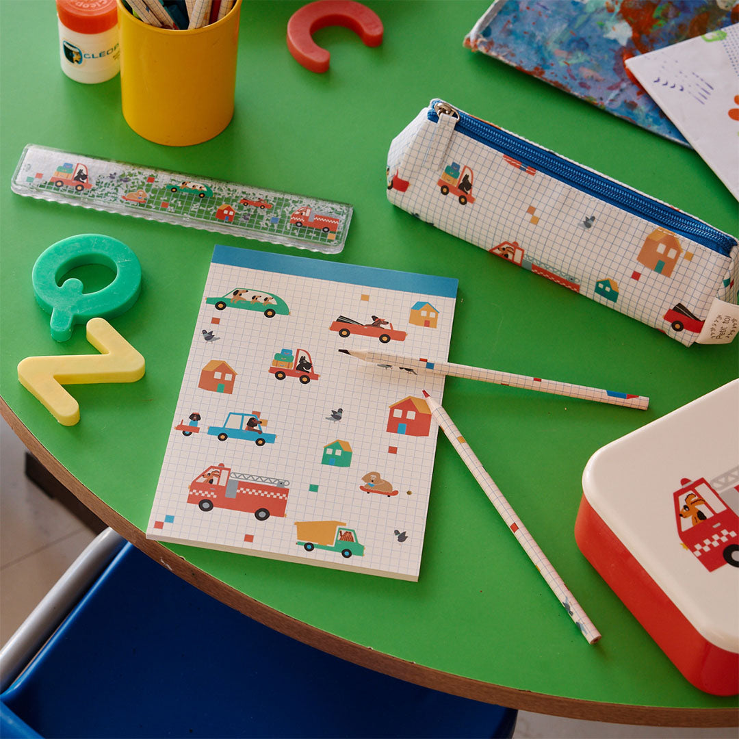 le petit souk schetsboek met voertuigen en honden, liggend op een groene tafel tussen bijpassende schoolspullen.