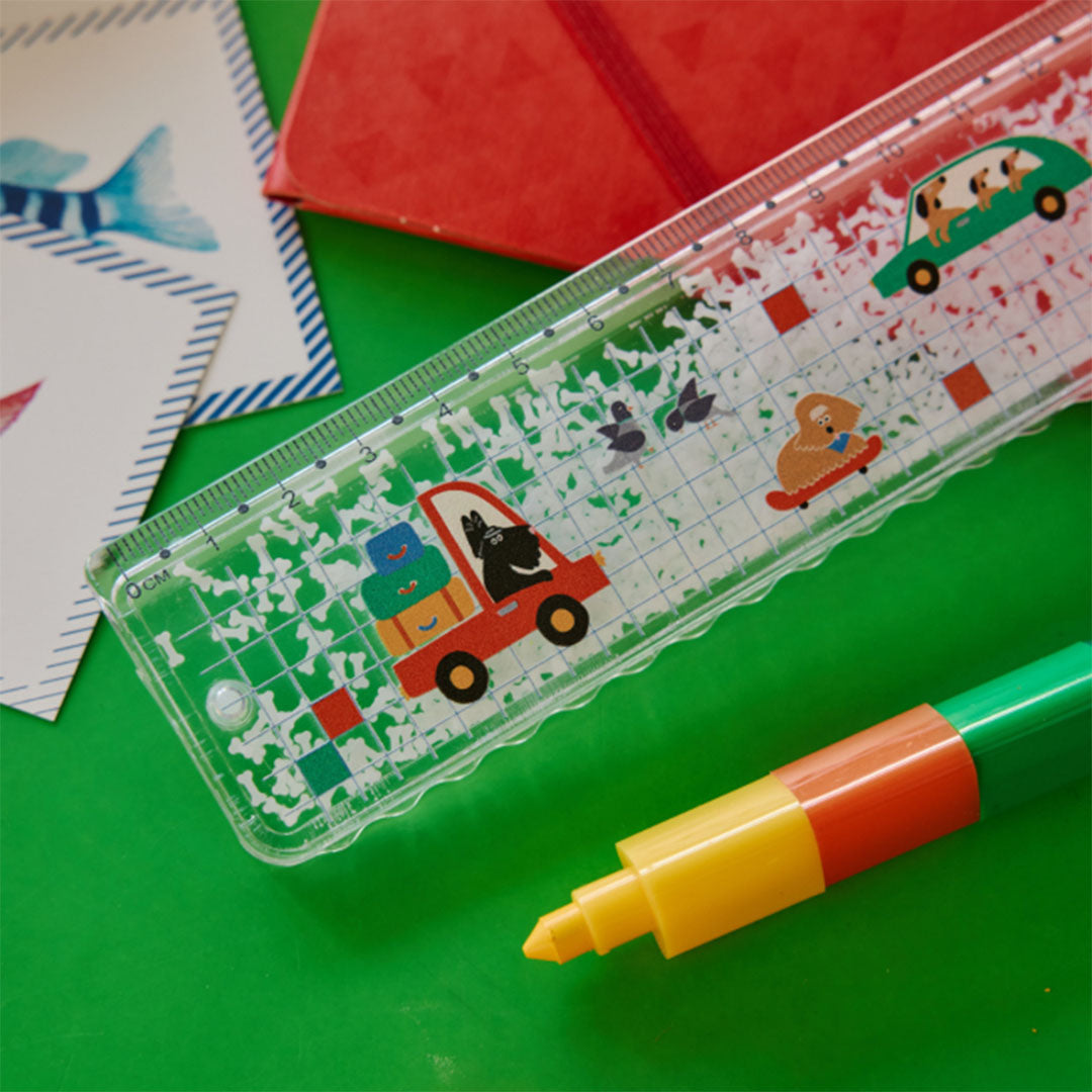 Le petit souk glitter liniaal met voertuigen en honden, schuin liggend op een groene ondergrond met een marker en notitieboek.