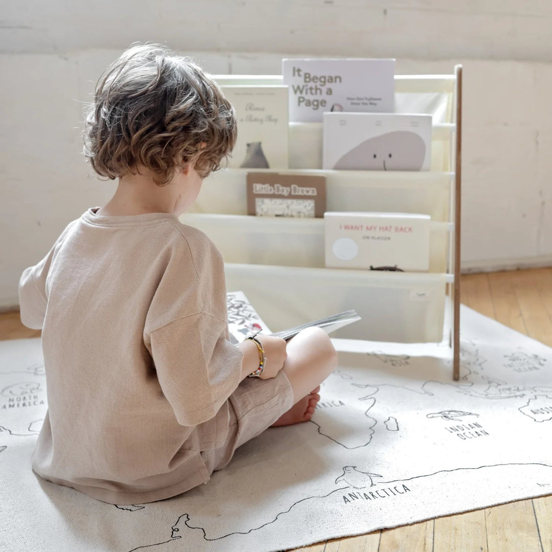 Een kind leest een boek voor een 3 sprouts kinderboekenrek gevuld met boeken.