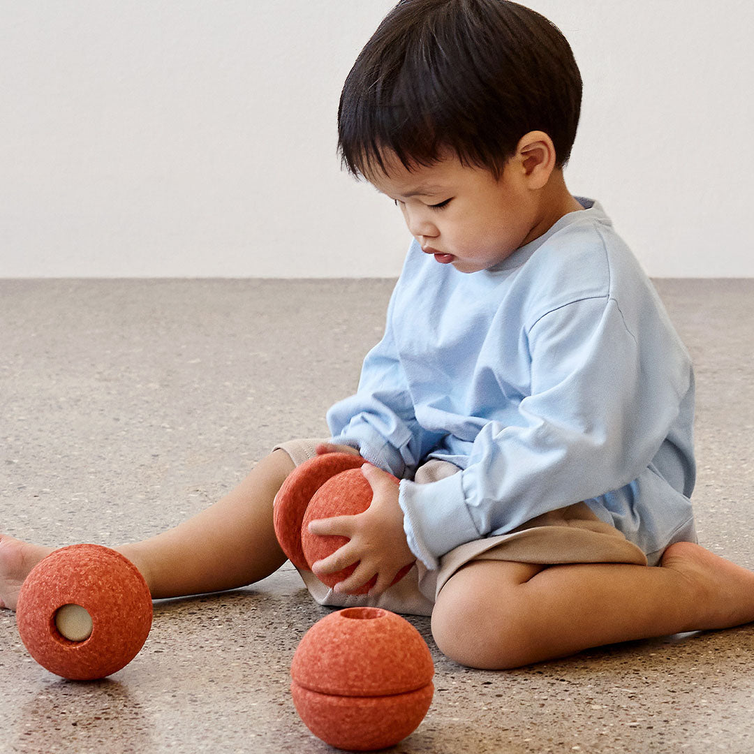 Een jong kind speelt op de grond met twee Modu burnt orange schuimrubber halve ballen.