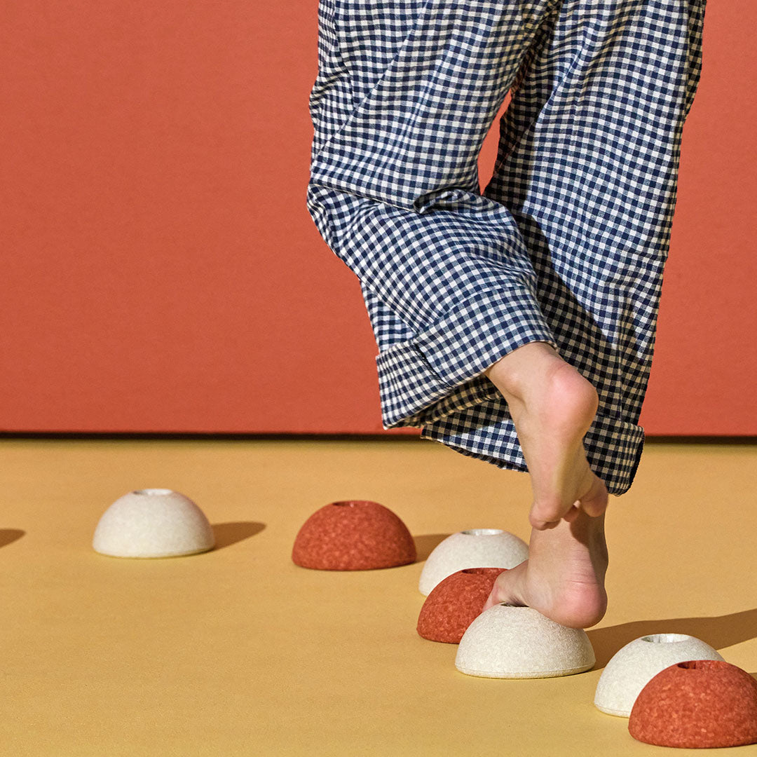 Een blote voet stapt op Modu burnt orange en witte schuimrubber halve ballen op een gele vloer.