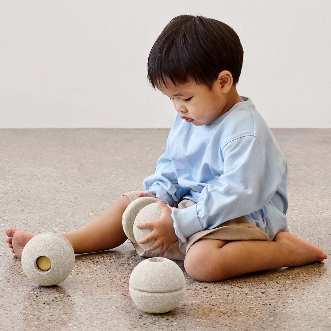 Een kind speelt zittend op de grond met twee Modu beige schuimrubber bouwballen.
