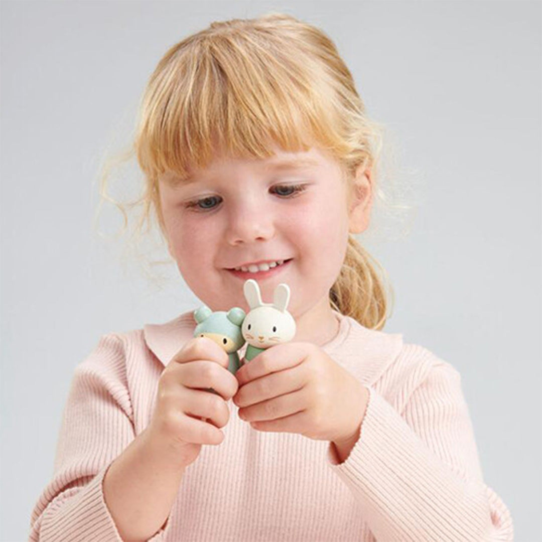 Een lachend kind houdt twee kleine Tender Leaf Toys houten konijnenfiguren vast.