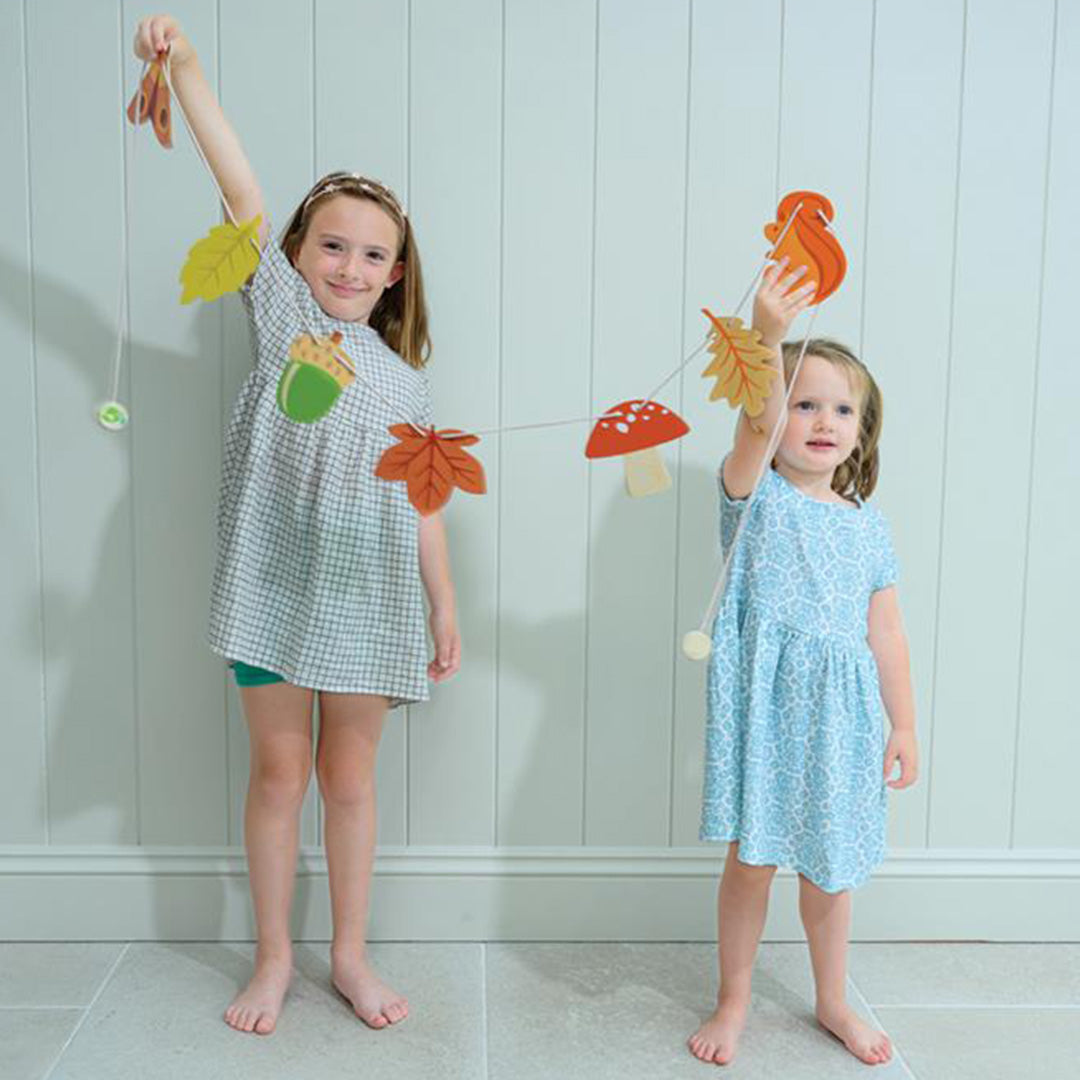 Twee meisjes houden de Tender Leaf Toys houten herfstslinger met bladeren en bosdieren vast.