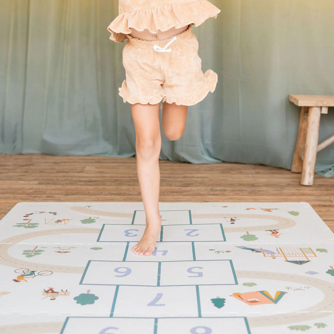 Een kind springt op blote voeten op de play&go speelmat met hinkelbaan.