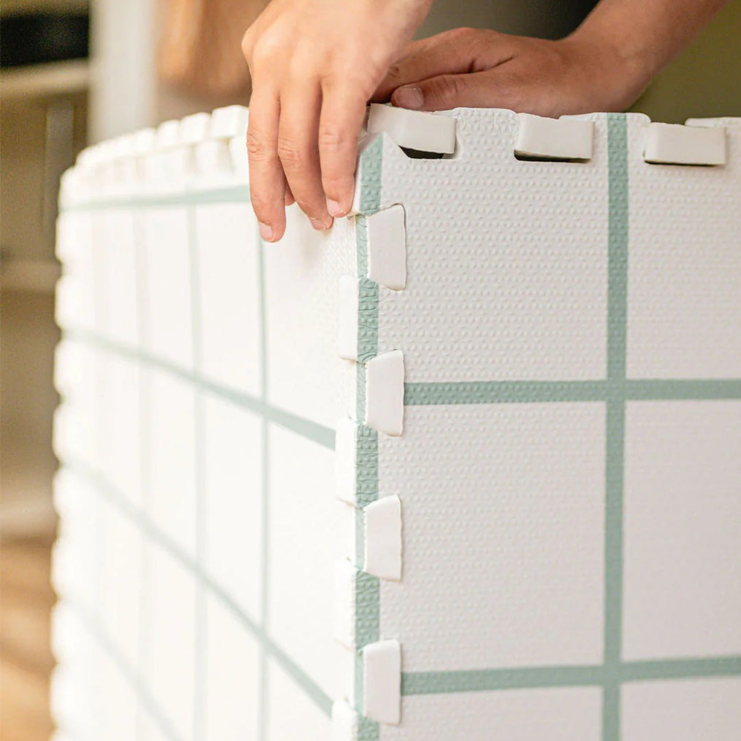 Close-up van handen die twee stukken van de play&go foam speelmat met rasterpatroon in elkaar klikken.
