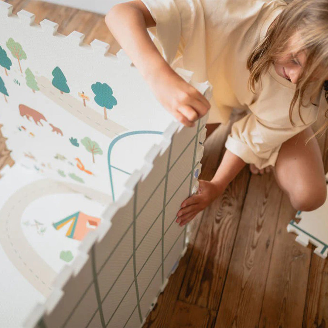 Een kind knielt en verbindt twee stukken van de play&go speelmat om een constructie te bouwen.
