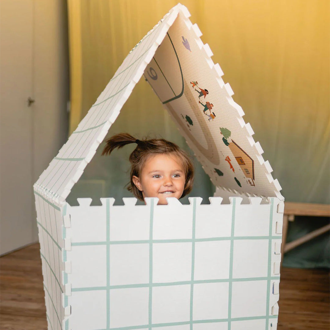 Een lachend kind kijkt uit een huisje gebouwd van de play&go foam speelmat.